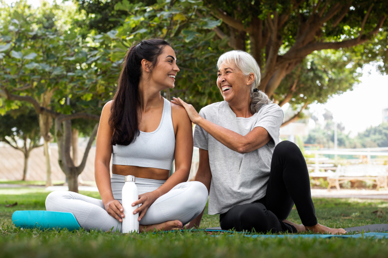 An older woman and younger woman sitting on yoga mats in a grassy area