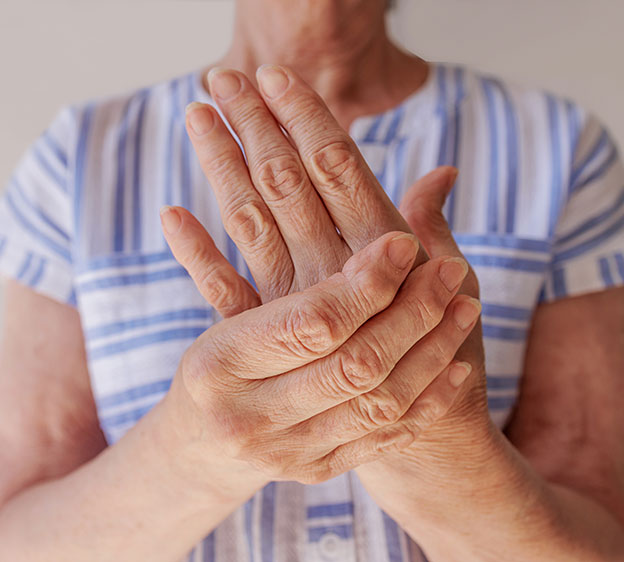 An older adult grabbing their left palm and hand with their right