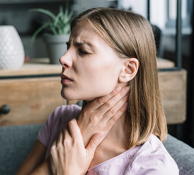 Close-up of a woman with discomfort, holding her upper throat with her hand and closing her eyes