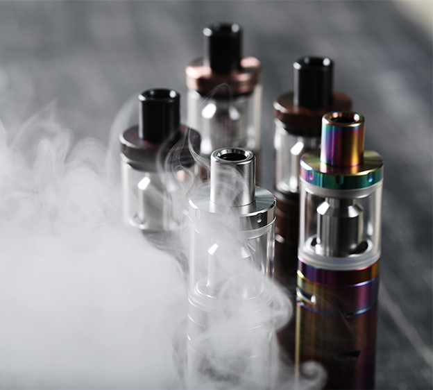 Five vaping devices or e-cigarettes in frame with smoke surrounding the foreground