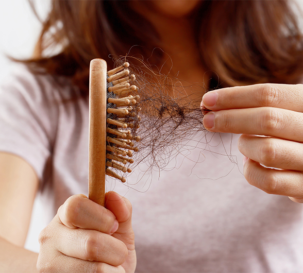 Photo of a young woman holding a wooden bristle hair brush in one hand and pulling tangled hair out of the bristles with the other