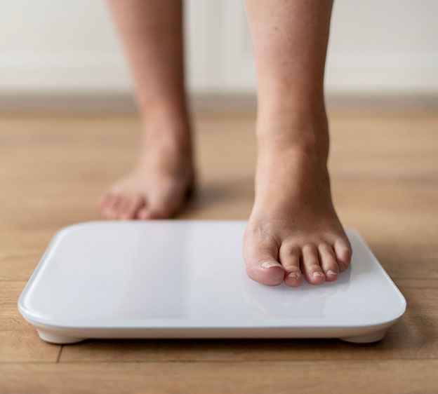 A person's feet standing on a white flat scale on a light wood floor