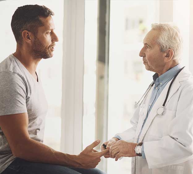 Health care provider and man looking at each other while having a discussion and the provider touches the patient’s finger tips