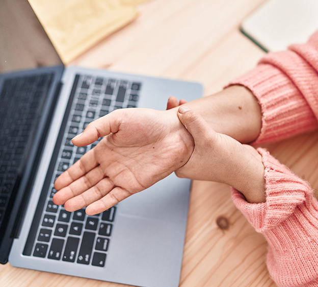 Younger adult woman holding her right wrist with her left hand over a laptop