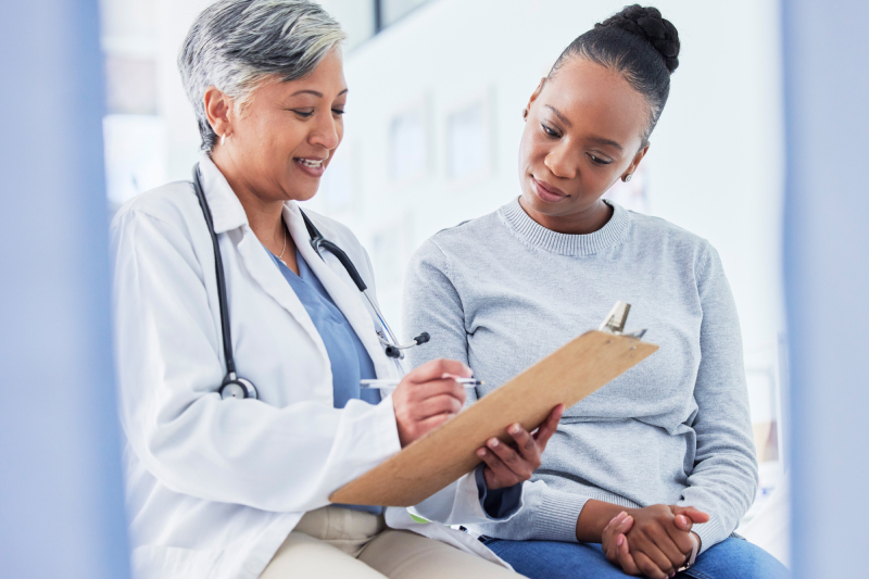 A medical provider and female patient sit side by side and look down at a clipboard