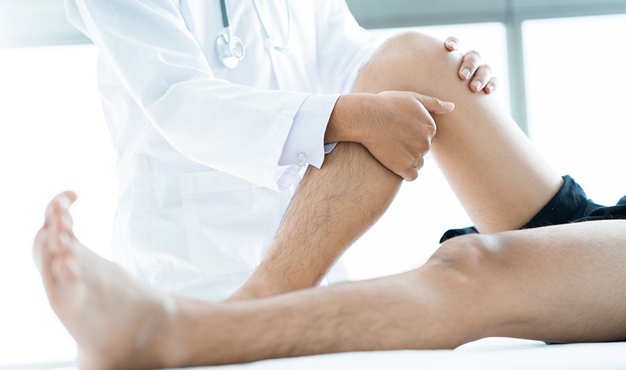 An unidentified doctor palpitates the right knee of an unidentified patient using both hands