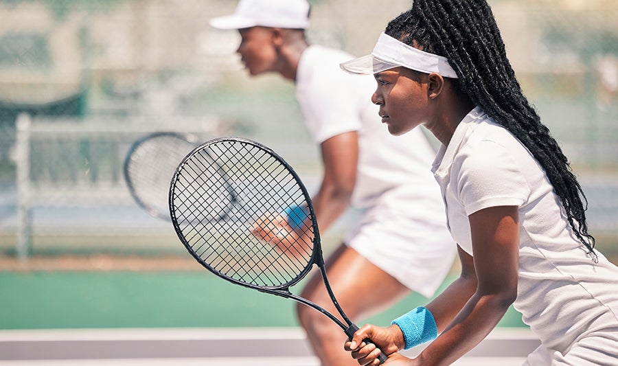 Younger woman gripping the handle of a tennis racket with both hands in a ready-stance.