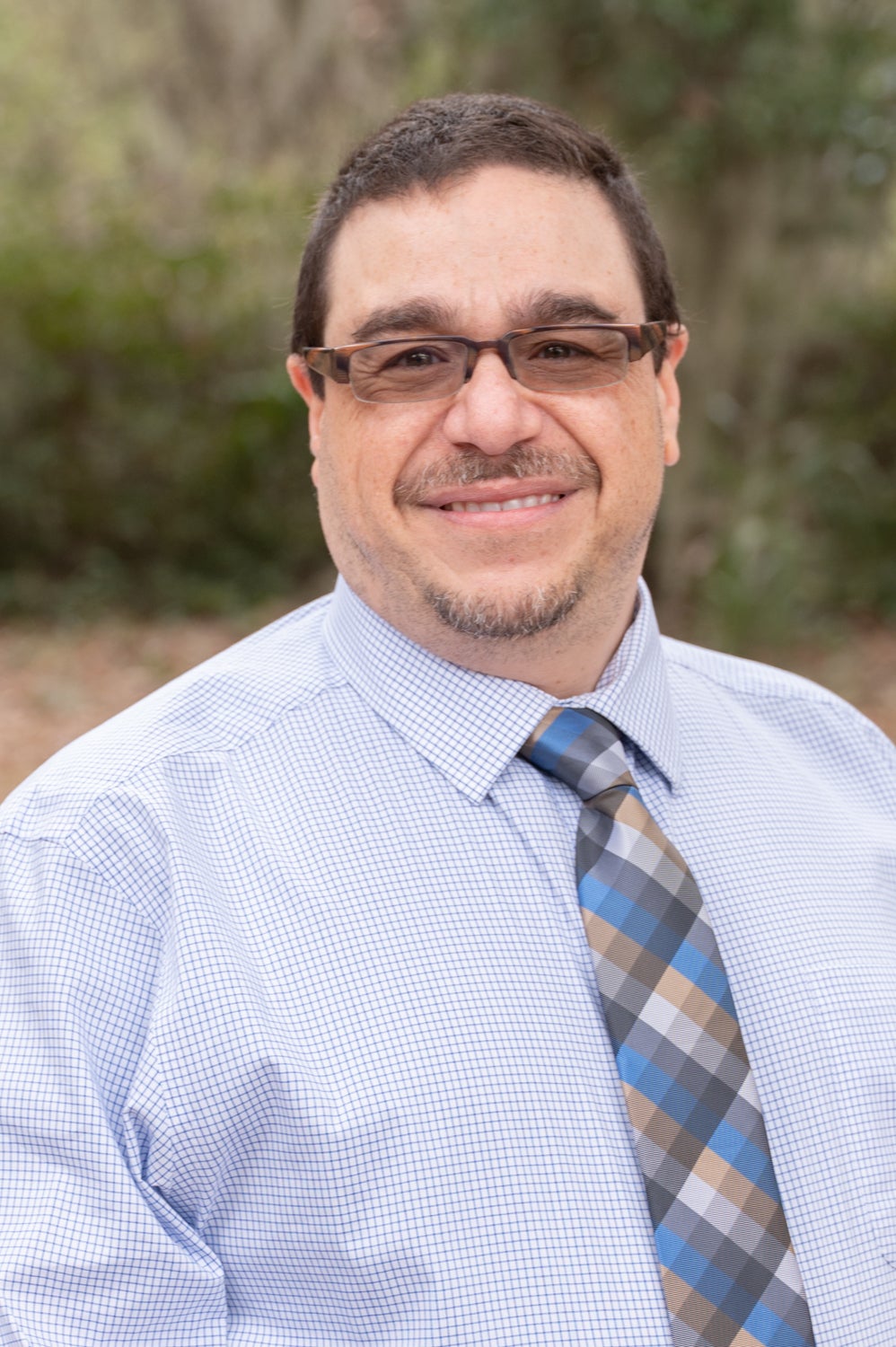 Dr. Joseph DiMaria in a blue patterned button down shirt and a checked multi-color tie in an outdoor setting.