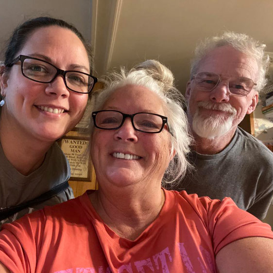 A woman named Beth Montana photographed with two other adults, all smiling and looking down toward the camera