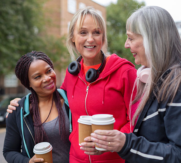 Three women standing together and laughing while holding coffee cups.