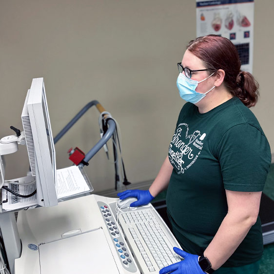 Jamie Harmon stands in front of a computer wearing a mask and purple nitrile gloves.