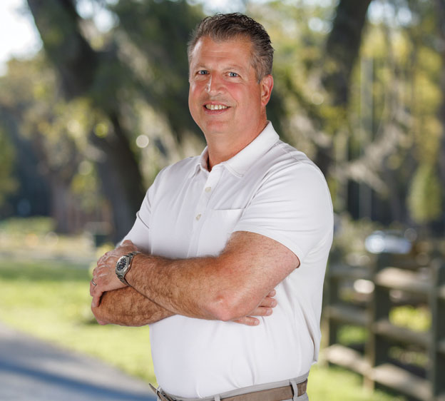 Dr. Michael Sciarra wearing a white polo T-shirt and crossing his arms and smiling while smiling toward the camera for a photograph