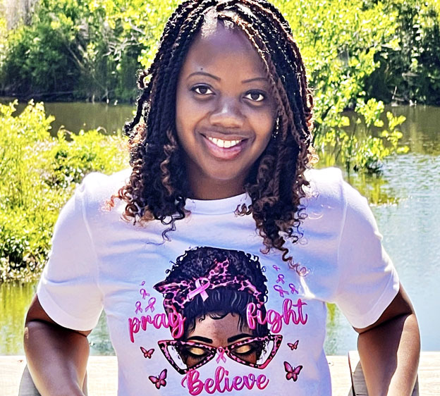 Breast cancer survivor Tiera White stands outdoors wearing a pink t-shirt decorated with pink breast cancer awareness ribbons.