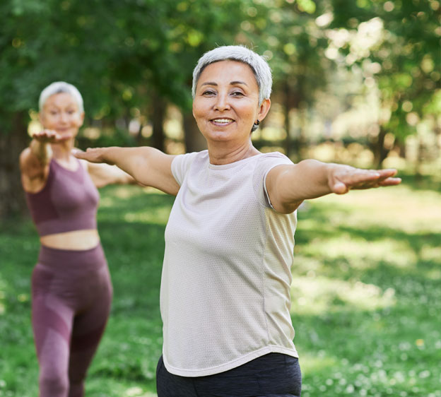 Two middle age women do yoga outdoors.