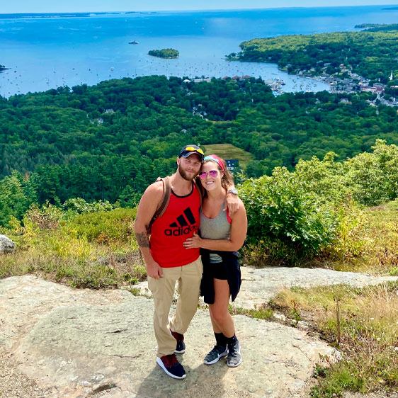 Tara Kay and her fiancé, Michael, stand on a cliff overlooking the ocean and an island below