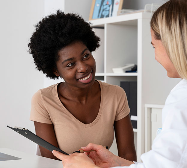 Younger Black woman smiling and speaking with a health care provider while looking at a chart.