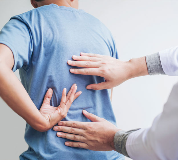 A provider examines a patient's back as the patient sits on an exam table.