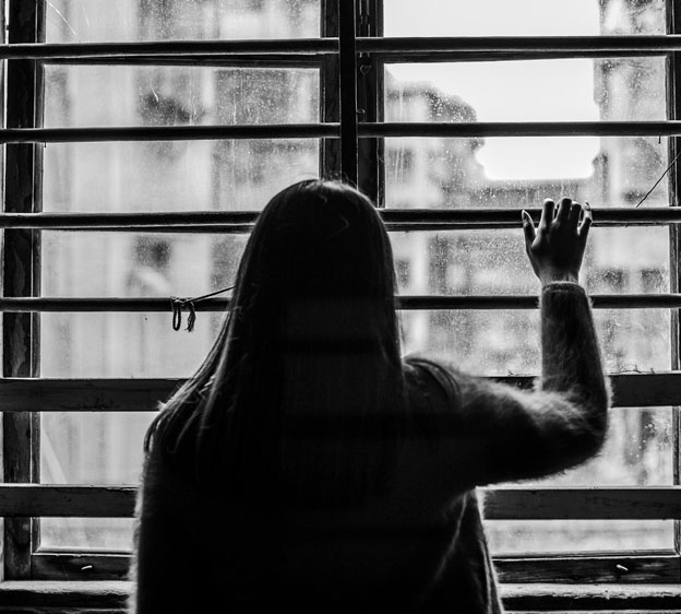 Woman in the shadows looking out the window through blinds