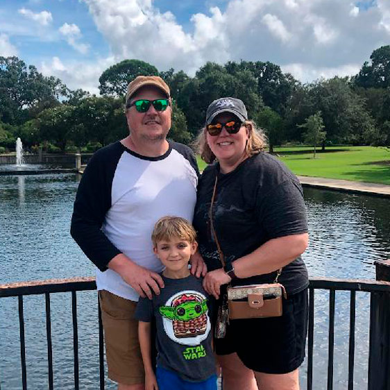 Luke Newman wears a Star Wars shirt and poses with his parents in front of a fountainy