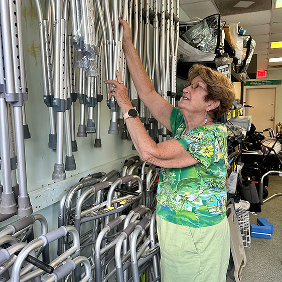 A woman named Carolyn Roos reaching up toward medical equipment hanging organized on a wall