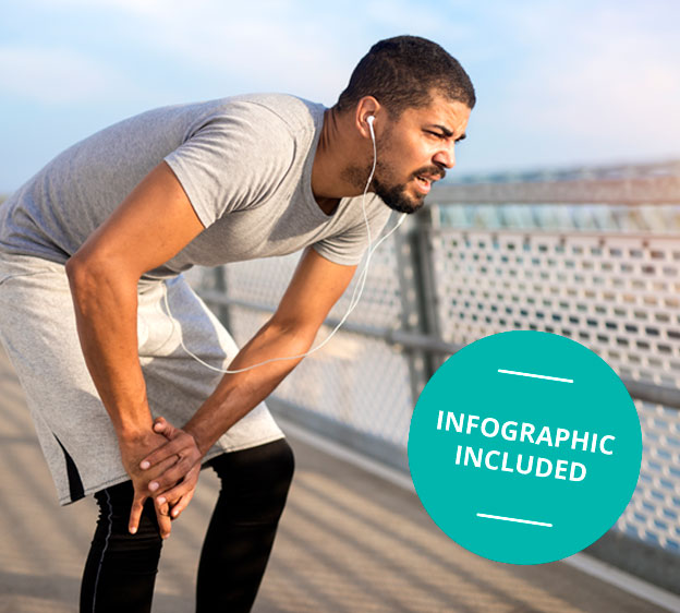 A young male runner stands on a bridge, bending over and holding his knee in pain.