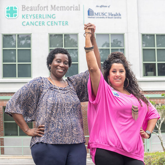 Breast cancer survivor Cheryl Fields and Kianna Brown, social worker, hold hands in the air and smile