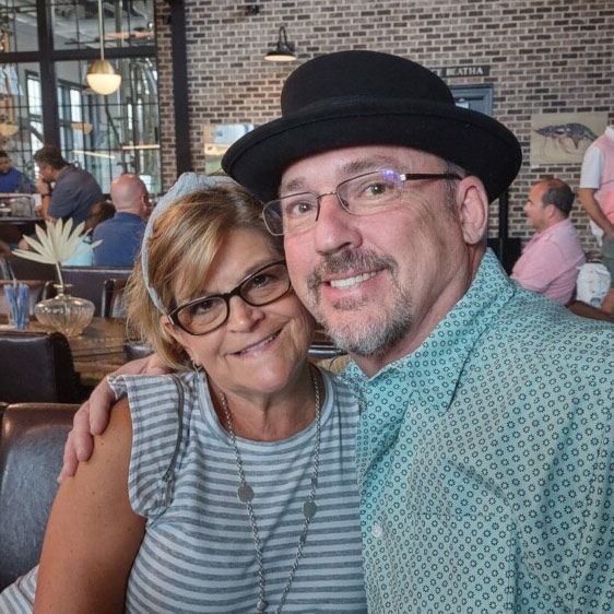 Beaufort Memorial Pharmacy Services Director Tim McCall wears a green checked shirt and bowler hat and has his around a woman wearing glasses, a blue and white striped shirt and a blue headband.