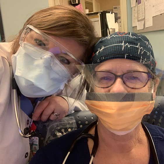 Two medical workers in scrubs and PPE photographed in a selfie