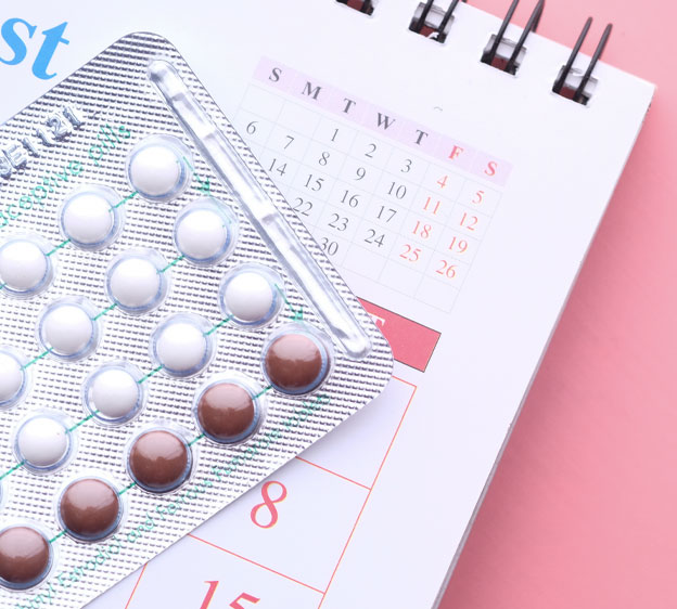 A packet of birth control pills on top of a monthly calendar