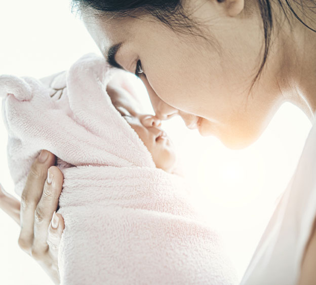 A young mother snuggling with her new baby, who is swaddled in a pink blanket