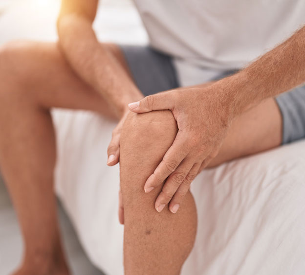 Person sitting on the edge of a bed holding their left knee