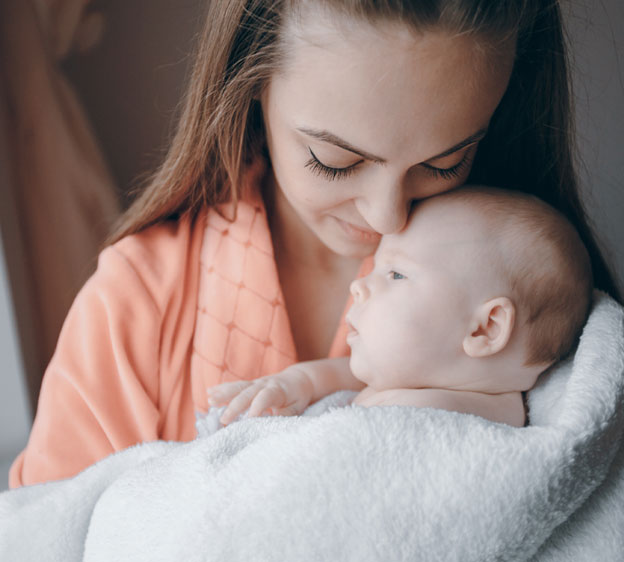 A young mother holds an infant wrapped in a blanket.