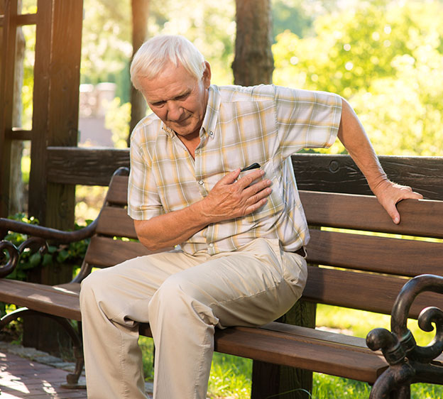 Older man sitting outside on a park bench clutching his chest