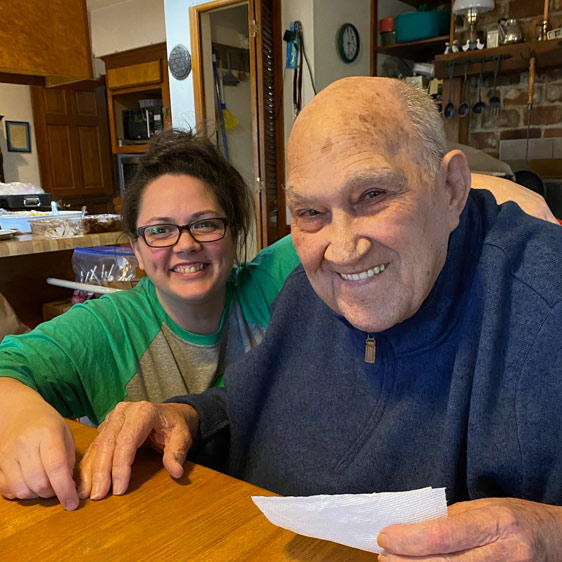 A woman named Beth Montana photographed with her grandfather while both are sitting at a wooden table