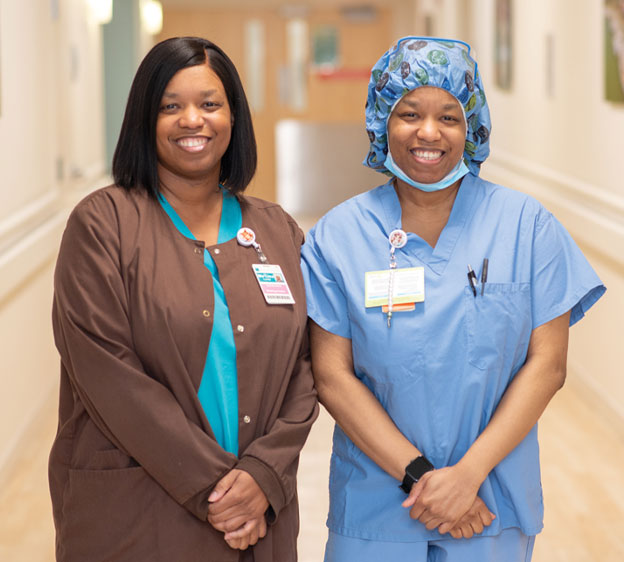 Me&rsquo;Lisa Lundy stands next to her twin sister, Me&rsquo;Tisha, who wears surgical scrubs, in a hallway at the Beaufort Memorial Collins Birthing Center.