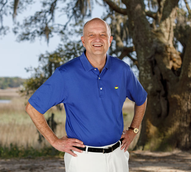 Dr. Michael Kaup stands outdoors in front of a live oak, hands on hips and smiling at the camera.