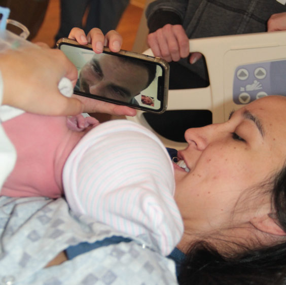 Claire Hardee holding her newborn while on a video call with her husband Ted