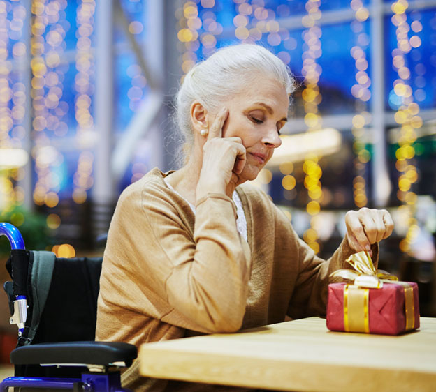 Older woman in a wheelchair sitting alone surrounded by holiday decorations