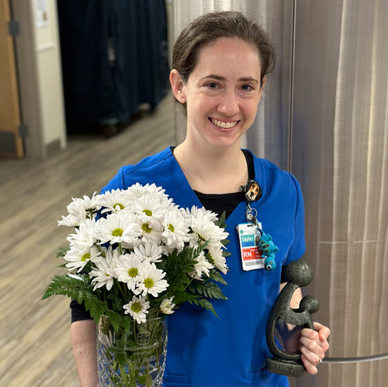 Nurse Practictioner Taylor Robinson photographed receiving the The DAISY Award for Extraordinary Nurses while holding a bouquet of white flowers