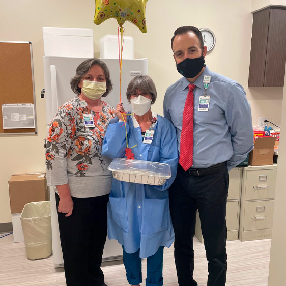 Three medical professionals wearing medical masks looking toward the camera while holding pans of food and other items