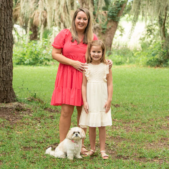 Ashley Gould Hutchison and her daughter Weslie photographed in front of a grassy area and smiling for the camera.