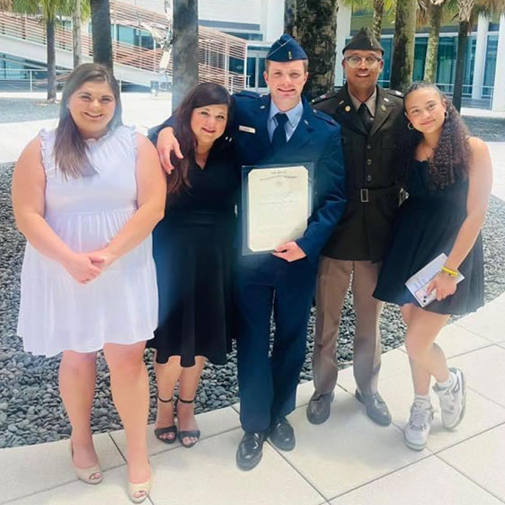 A group of five people with one of them in military uniform and holding a diploma