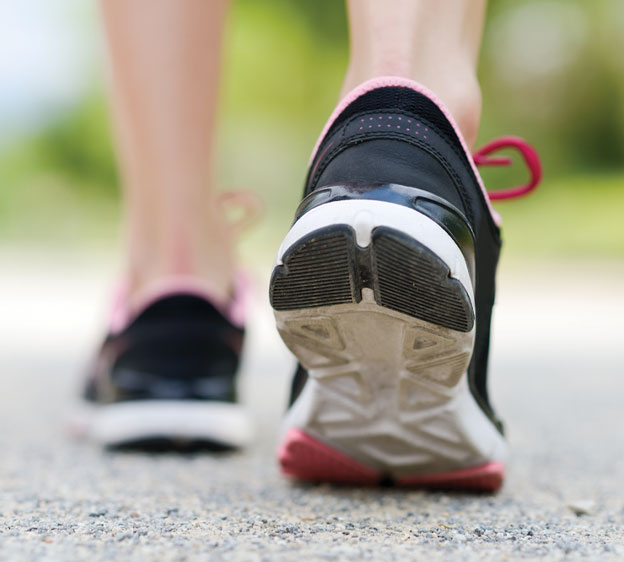 A photo of the back of someone&rsquo;s feet while they are walking and wearing black and white tennis shoes with red laces.