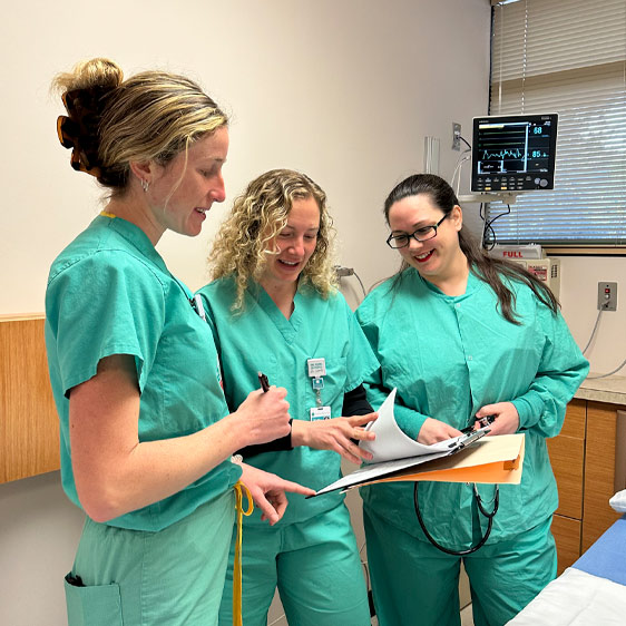 A photograph of three woman in teal hospital scrubs in a medical room