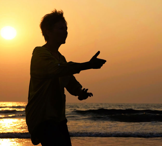 Older adult performing tai chi on the beach during sunset