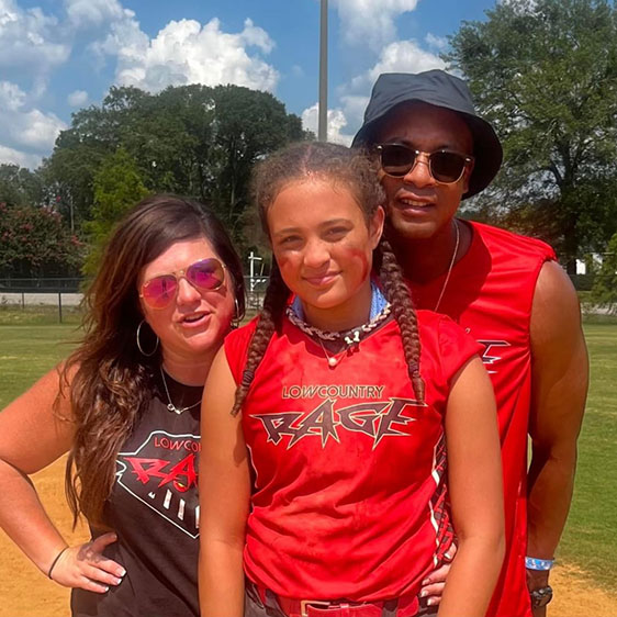 Two adults and a child wearing matching red shirts photographed at a sports field