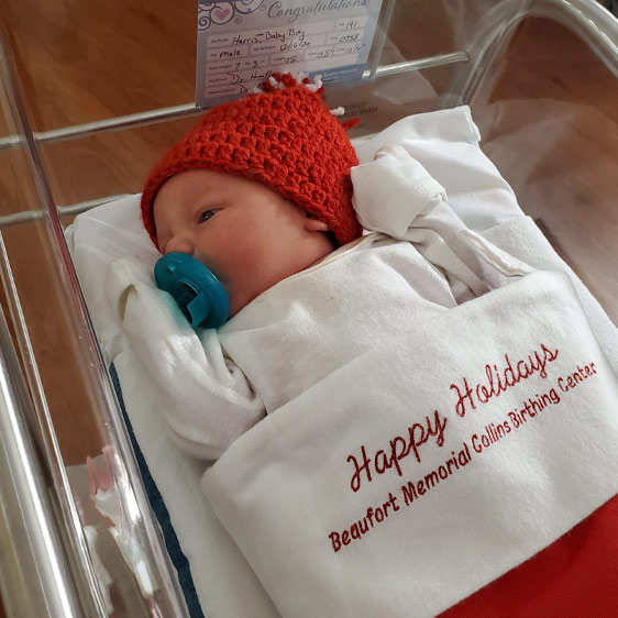 A photo of a newborn wrapped in a stocking that says Happy Holidays, Beaufort Memorial Collins Birthing Center