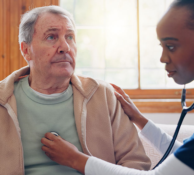 A medical professional listening to an older man&rsquo;s heart with a stethoscope.