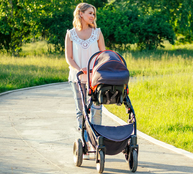 Young mother walking in a park pushing a baby stroller