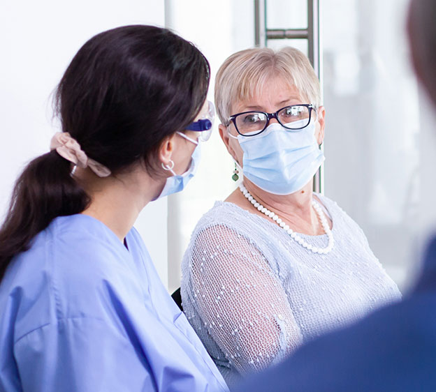 A woman wearing a mask listens to another woman at a cancer support group